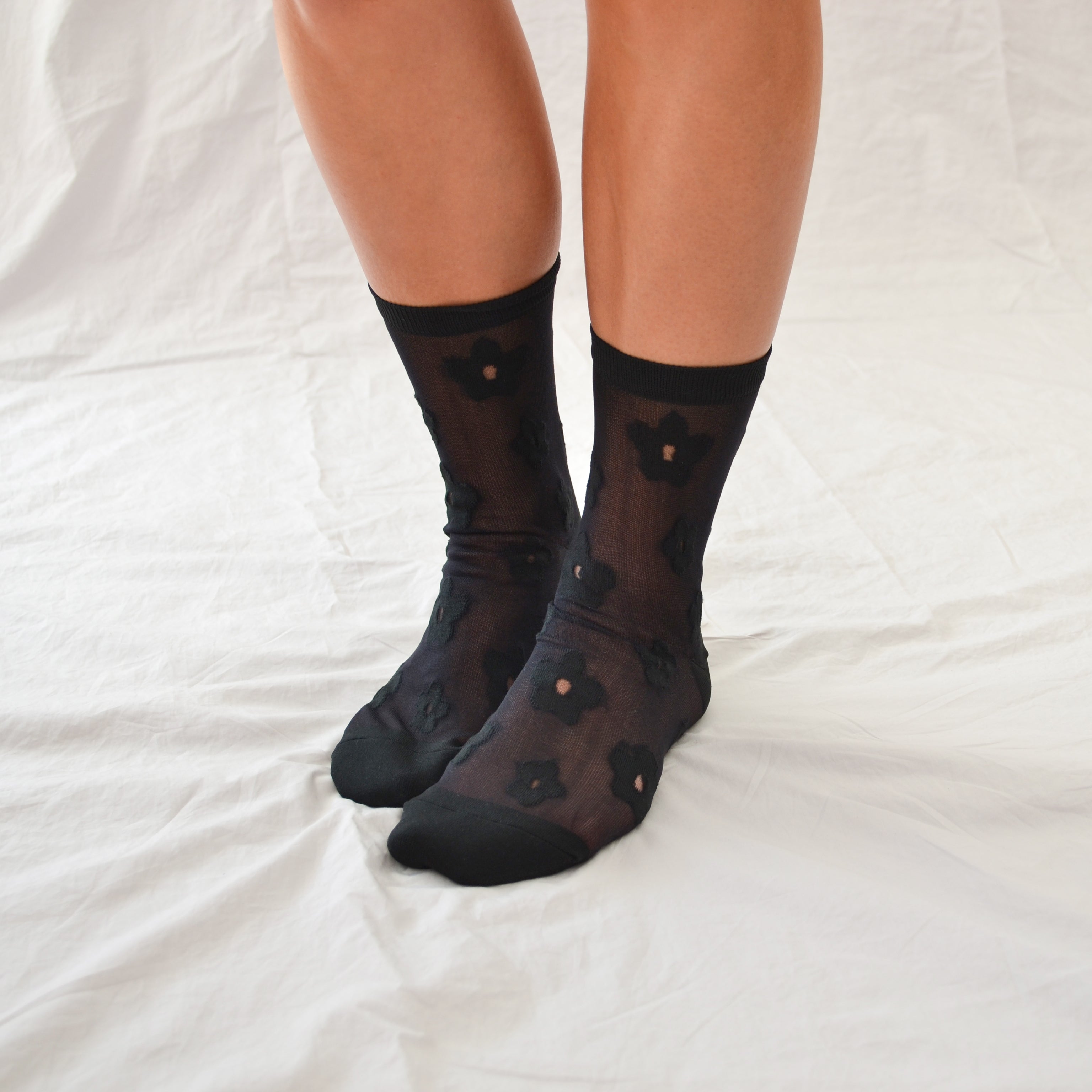 Classic sheer socks in black or white with a delicate floral pattern, solid heels, toes, and a shorter crew length.