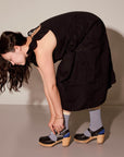 Woman in a black dress tying her shoes against a plain background