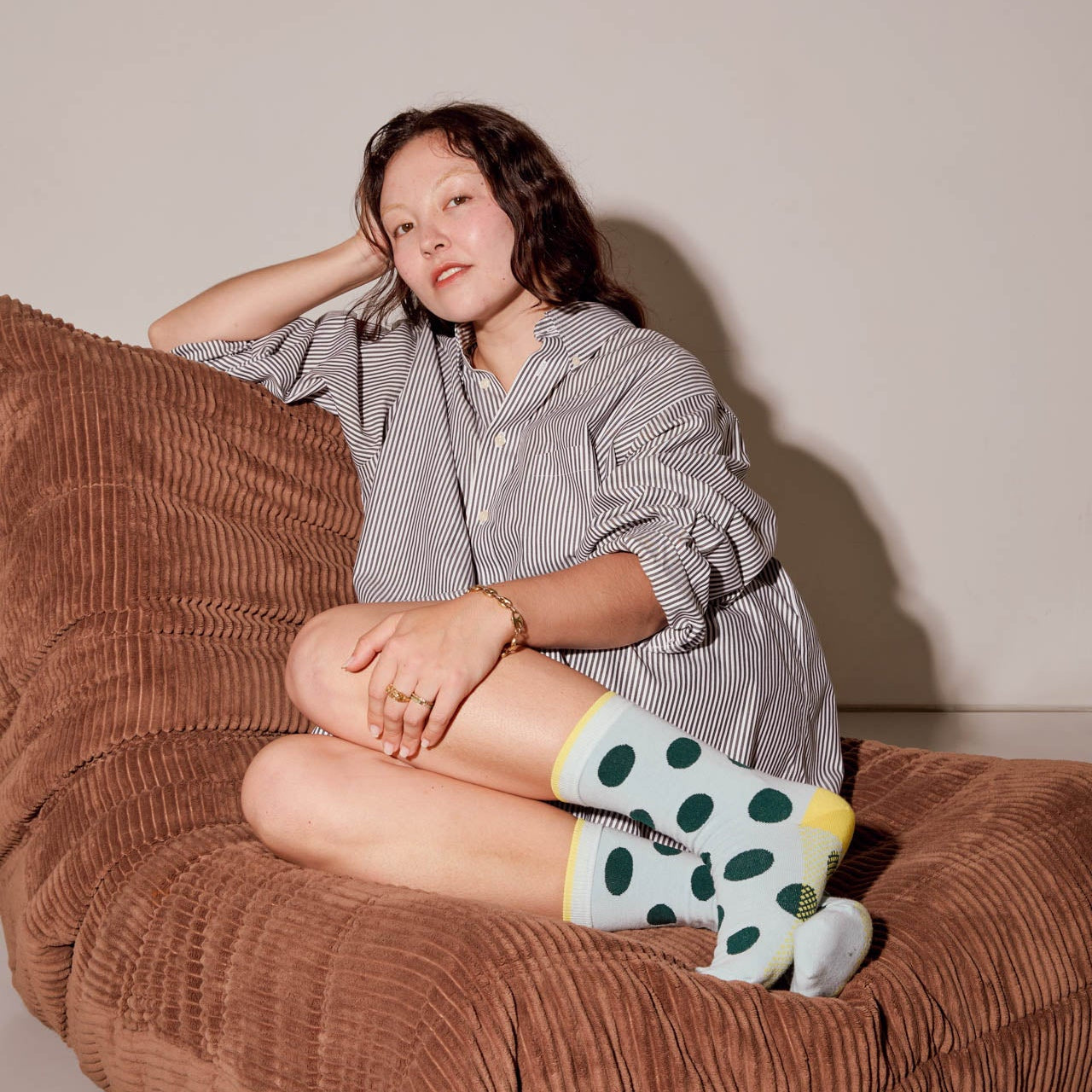 Person sitting on a brown bean bag chair wearing a checkered shirt and polka dot socks.